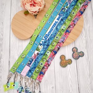 Puede incluir: Una colección de cordones con diseños de la película "Monstruos, S.A." en tonos verdes, azules y rosas. Los cordones tienen colgantes adjuntos y detalles brillantes con forma de Mickey Mouse. El texto "Monsters, Inc." es visible en un cordón.