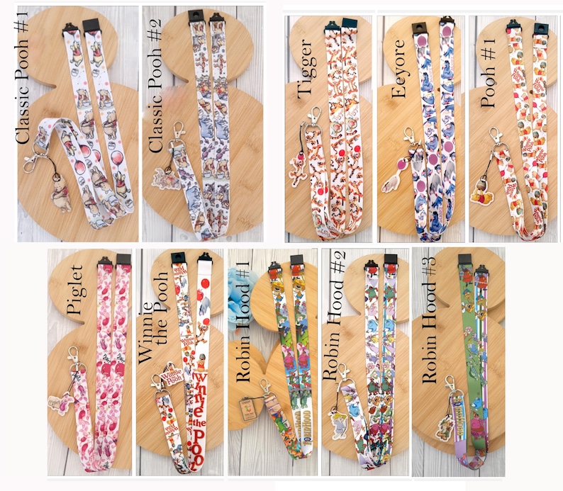 May include: A collection of ten fabric lanyards featuring various character prints including Winnie the Pooh, Tigger, Eeyore, Piglet, and Robin Hood. Each lanyard includes a metal lobster clasp and a matching character charm attached to the end.