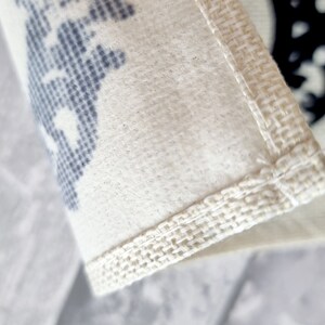 May include: Close-up of a white fabric bag with a blue and white patterned design. The bag has a white fabric trim around the edges.