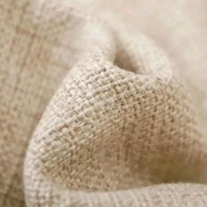 May include: Close-up of a beige linen fabric with a woven texture. The fabric is soft and has a natural, rustic look.