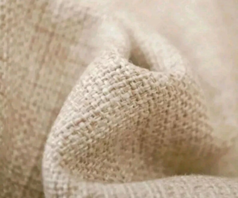 May include: Close-up of a beige linen fabric with a woven texture. The fabric is soft and has a natural, rustic look.