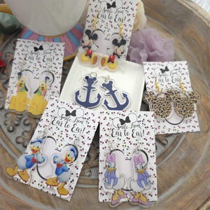 May include: Five pairs of acrylic dangle earrings on white display cards with the text Smile from Ear to Ear. Designs include Mickey Mouse, Pluto, navy blue anchors, leopard print Mickey ears, Donald Duck, and Daisy Duck with gold or silver hooks.