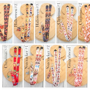 May include: A collection of nine fabric lanyards featuring various holiday-themed patterns including Halloween pumpkins, Christmas characters, nutcrackers, and gingerbread designs. Each lanyard includes a metal lobster clasp and a small acrylic charm.