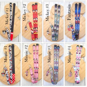 May include: A collection of eight fabric lanyards featuring various Disney character prints including Mickey Mouse, Minnie Mouse, and Fantasia. Each lanyard includes a black plastic buckle, a metal lobster clasp, and a clear acrylic character charm.