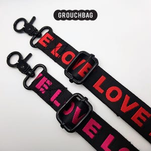 May include: Two black adjustable straps with metal clasps. One strap has the word "LOVE" printed in red, and the other strap has the word "LOVE" printed in pink.