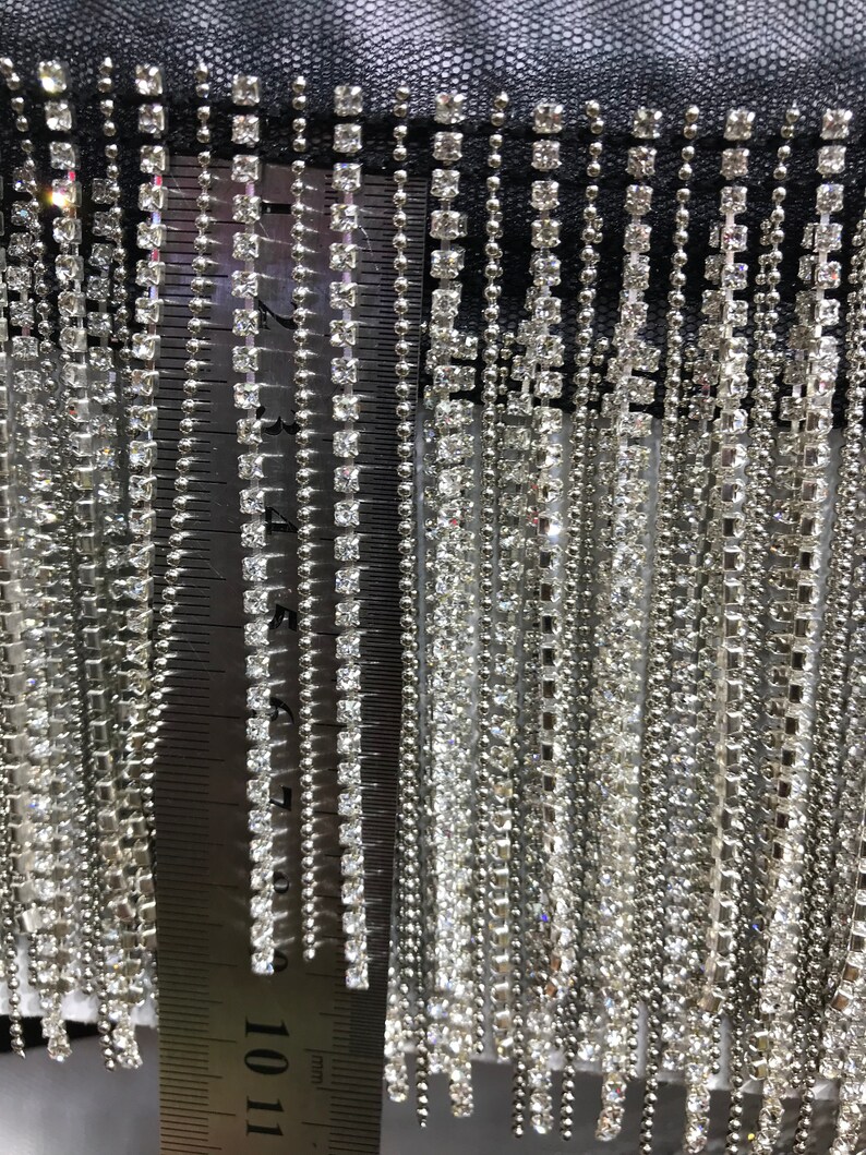 May include: Close-up of silver fringe trim with clear rhinestones. The fringe is approximately 11 inches long.