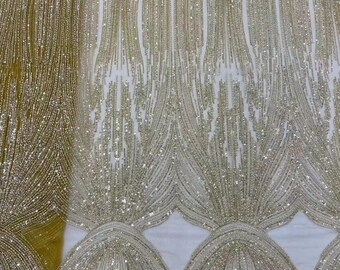 May include: A close-up of a gold beaded fabric with a shimmering, iridescent finish. The fabric features a repeating pattern of vertical lines and arches.