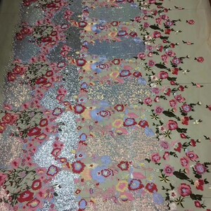 May include: A close-up of a silver and pink fabric with floral embroidery and sequins. The fabric has a delicate, sheer texture and is perfect for creating elegant garments or accessories.
