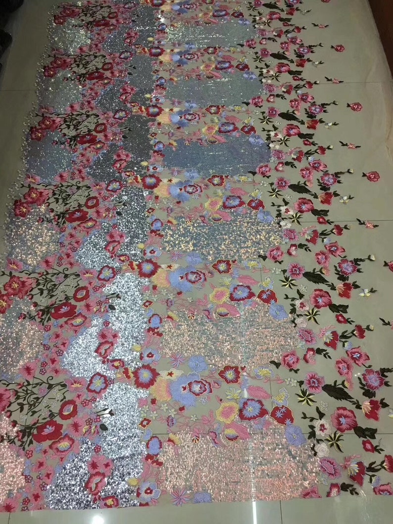 May include: A close-up of a silver and pink fabric with floral embroidery and sequins. The fabric has a delicate, sheer texture and is perfect for creating elegant garments or accessories.
