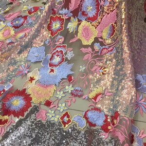 May include: A sheer fabric with embroidered floral designs in shades of red, pink, blue, yellow, and green. The fabric is embellished with iridescent sequins.