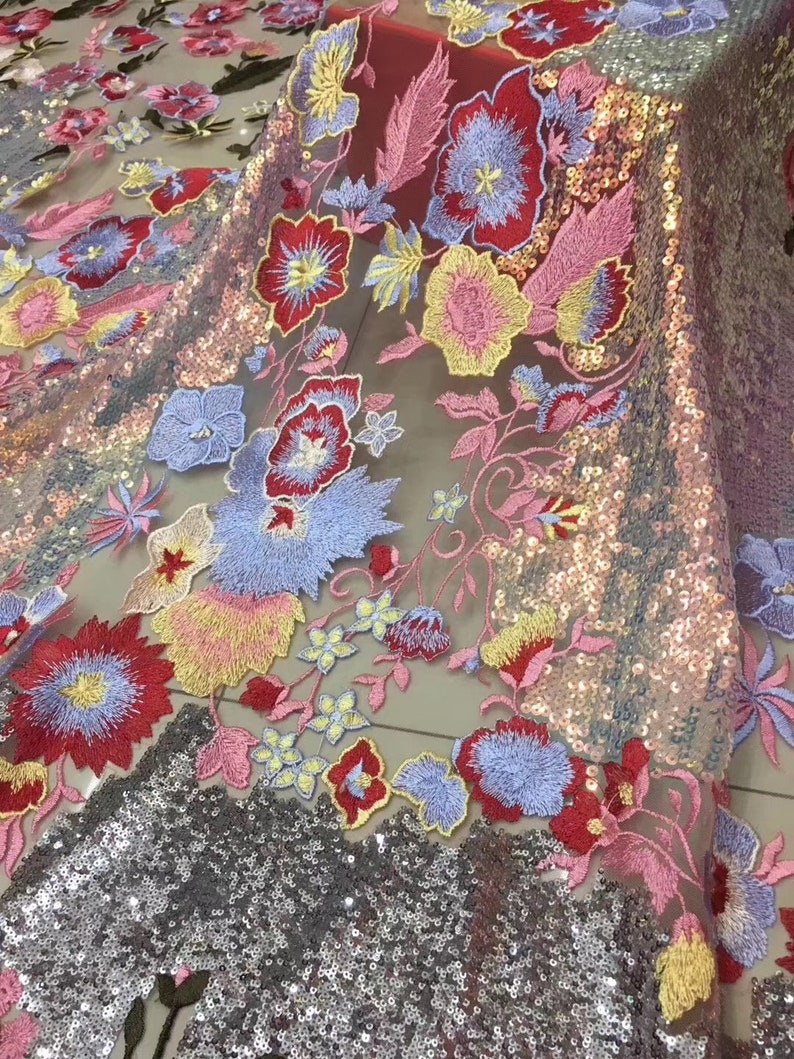 May include: A sheer fabric with embroidered floral designs in shades of red, pink, blue, yellow, and green. The fabric is embellished with iridescent sequins.