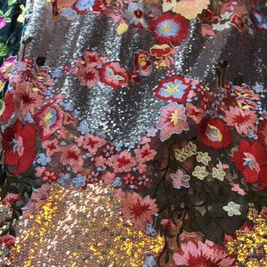 May include: A close-up of a fabric with a shimmering gold and silver sequin background and a floral embroidery pattern in shades of pink, red, blue, and yellow.