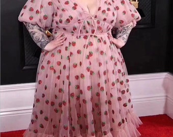 May include: A pink tulle dress with a strawberry print and a V-neckline. The dress has puff sleeves and a ruffled hem.