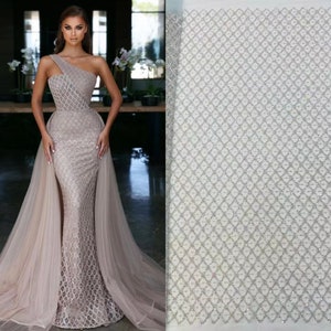 May include: A silver sequined fabric with a diamond pattern. The fabric is sheer and has a delicate texture.