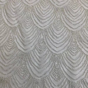 May include: White fabric with a beaded pattern of overlapping scallops. The beads are small and create a delicate, intricate design.