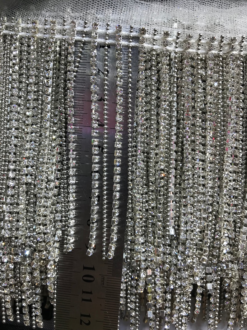 May include: Close-up of a silver trim with a fringe of clear rhinestones. A ruler is visible in the image, showing the trim is approximately 12 inches long.