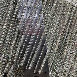 May include: Close-up of a silver chain trim with square rhinestones. The chain is measured with a ruler showing 11 centimeters.