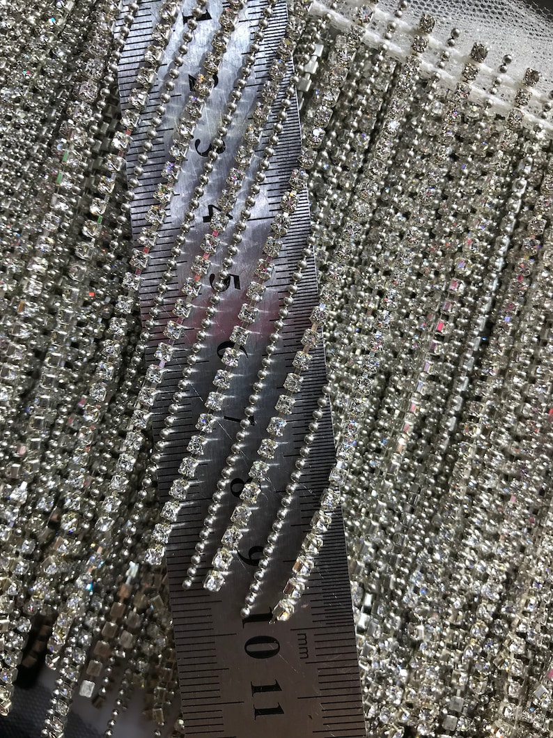May include: Close-up of a silver chain trim with square rhinestones. The chain is measured with a ruler showing 11 centimeters.