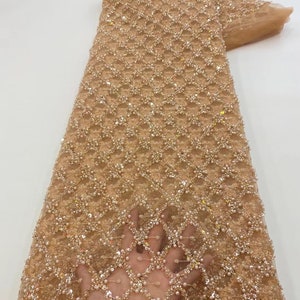 May include: Beige beaded lace fabric with a geometric pattern. The fabric is embellished with sequins and pearls.