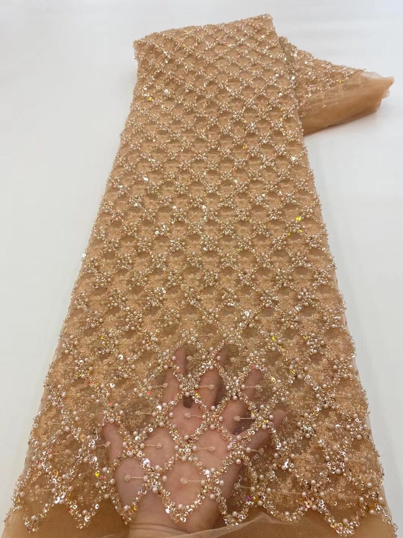 May include: Beige beaded lace fabric with a geometric pattern. The fabric is embellished with sequins and pearls.