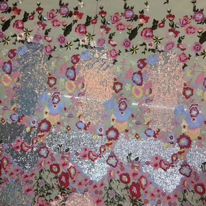 May include: A silver sequined fabric with embroidered floral designs in shades of pink, red, blue, and yellow. The fabric has a glittery finish and is perfect for crafting or sewing projects.