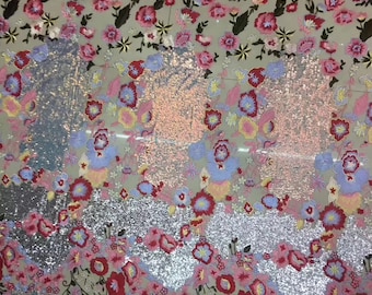 May include: A silver sequined fabric with embroidered floral designs in shades of pink, red, blue, and yellow. The fabric has a glittery finish and is ideal for crafting or sewing projects.