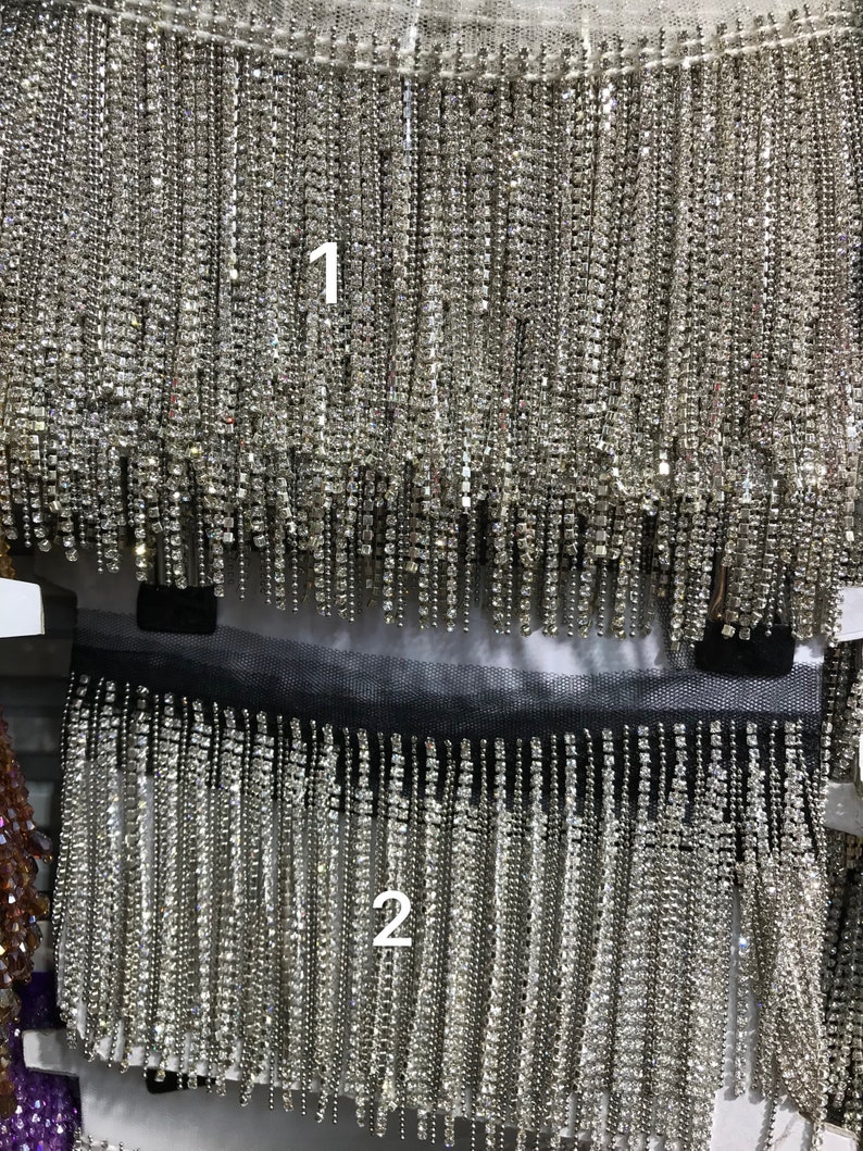 May include: Two rows of silver fringe trim with clear rhinestone embellishments. The fringe is approximately 1 inch long. The trim is perfect for adding a touch of sparkle to any project.