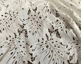 May include: White cotton fabric with a delicate, intricate lace pattern of leaves. The fabric is lightweight and sheer, with a soft, flowing texture.