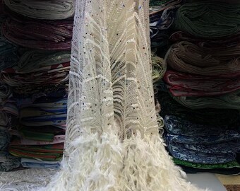 May include: White beaded and feathered lace fabric with a delicate floral pattern. The fabric has a sheer, lightweight texture and is adorned with iridescent sequins and white feathers.