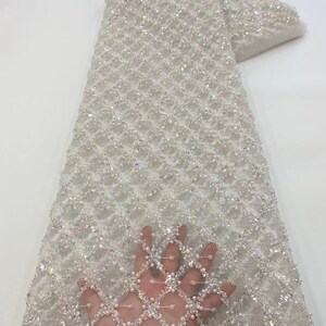 May include: White beaded lace fabric with a diamond pattern. The fabric is embellished with iridescent sequins and pearls.