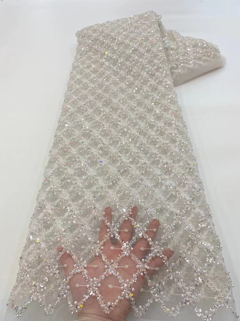 May include: White beaded lace fabric with a diamond pattern. The fabric is embellished with iridescent sequins and pearls.