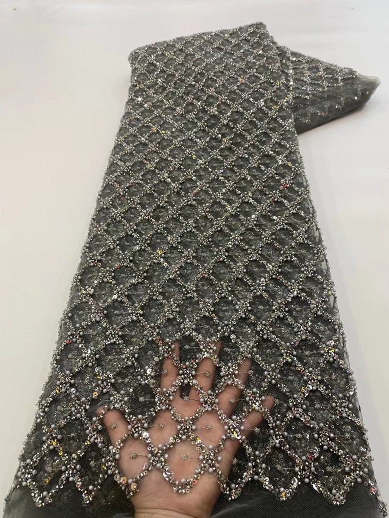 May include: Gray beaded lace fabric with a geometric pattern. The fabric is embellished with silver beads and sequins.