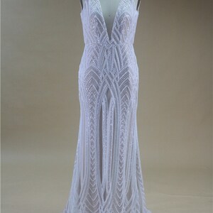 Puede incluir: Un vestido blanco sin mangas con un escote en V profundo y un patr&oacute;n geom&eacute;trico de lentejuelas. El vestido tiene un corpi&ntilde;o ajustado y una falda fluida.