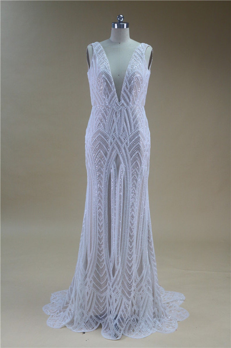 Puede incluir: Un vestido blanco sin mangas con un escote en V profundo y un patr&oacute;n geom&eacute;trico de lentejuelas. El vestido tiene un corpi&ntilde;o ajustado y una falda fluida.