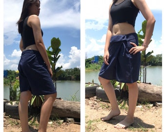 Pode incluir: Calções envolventes azul marinho. Os calções são até ao joelho e têm um design envolvente. São feitos de um tecido texturizado. A modelo está a usar um top preto curto. O fundo inclui um lago e céu azul.
