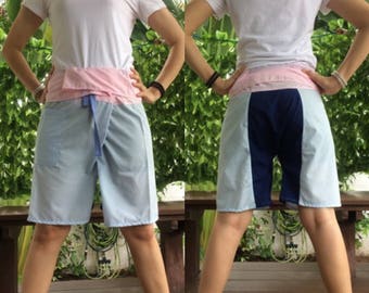 May include: A pair of light blue shorts with a pink and navy blue waistband. The shorts are tied at the waist with a blue string. The shorts are shown from the front and back.