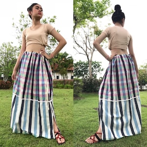 以下が含まれることがあります： ピンク、グリーン、ブラックのチェック柄のロングスカート。スカートは裾に白いストライプ柄があり、サイドにスリットが入っています。