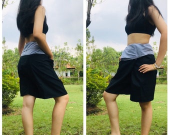 Pode incluir: Shorts pretos de envolver com uma cintura listrada cinza e branca. Os shorts são mostrados em uma pessoa em pé em uma área gramada.