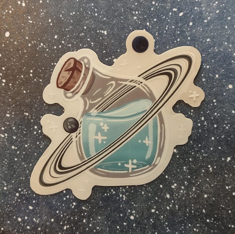 May include: A sticker featuring a potion bottle with a cork stopper, surrounded by a planet's rings. The bottle contains a teal liquid with cross-shaped sparkles. The sticker has a white border and is set against a starry background.