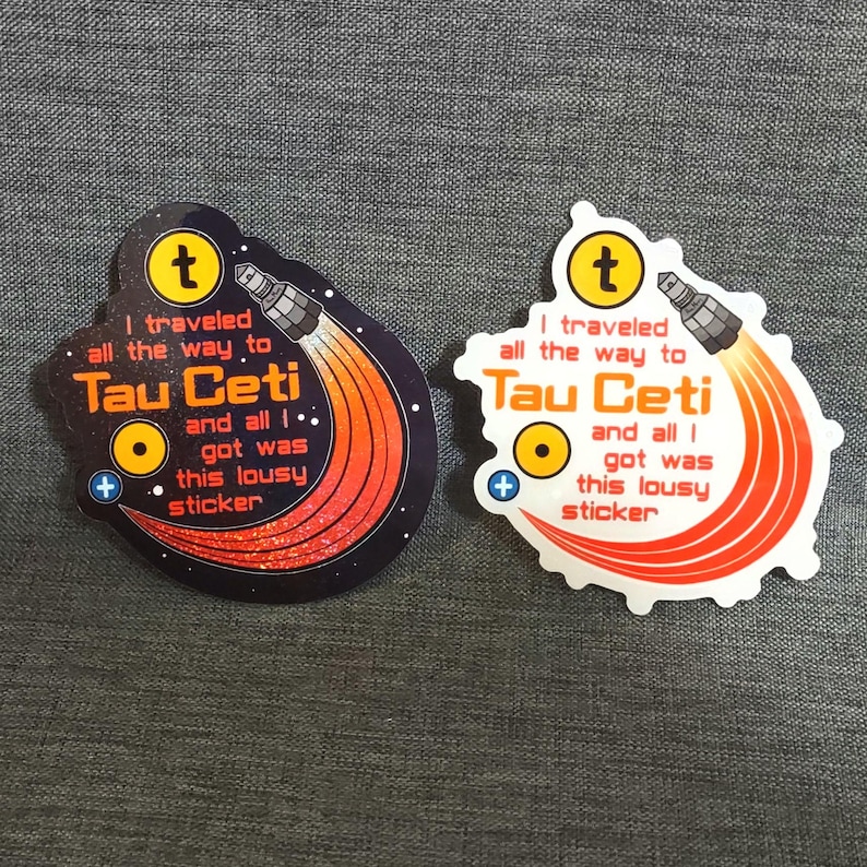 Puede incluir: Dos pegatinas con tem&aacute;tica espacial. Cada pegatina presenta un cohete con llamas naranjas y rojas, el texto "I traveled all the way to Tau Ceti and all I got was this lousy sticker" y un c&iacute;rculo amarillo con un signo m&aacute;s.