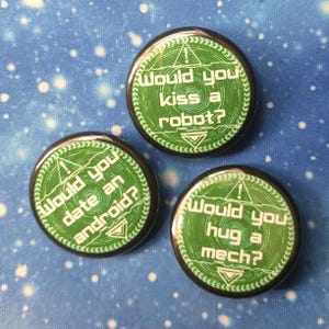 May include: Three circular badges with black edges and green and white text. Each badge poses a question: "Would you kiss a robot?", "Would you date an android?", and "Would you hug a mech?" They are set against a blue background with white dots.