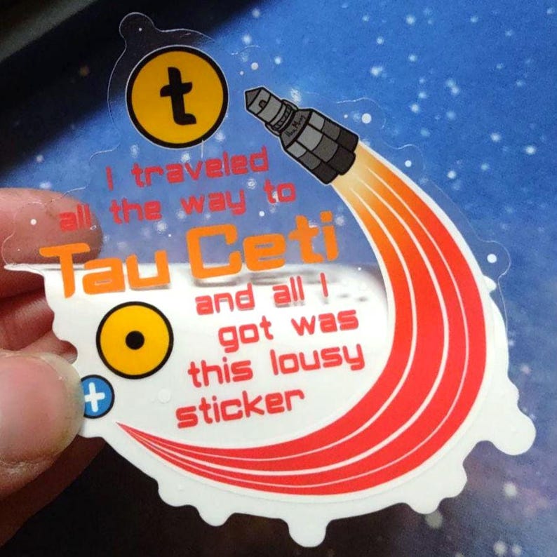 Puede incluir: Una pegatina transparente con un dise&ntilde;o de cohete y el texto "I traveled all the way to Tau Ceti and all I got was this lousy sticker." El dise&ntilde;o utiliza colores naranja y amarillo.