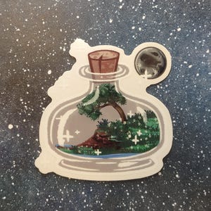May include: A sticker featuring a whimsical scene inside a glass bottle. The bottle contains a miniature landscape with a tree, water, and greenery. A cork seals the bottle, and a moon graphic is attached. The sticker has a white border and is set against a starry background.