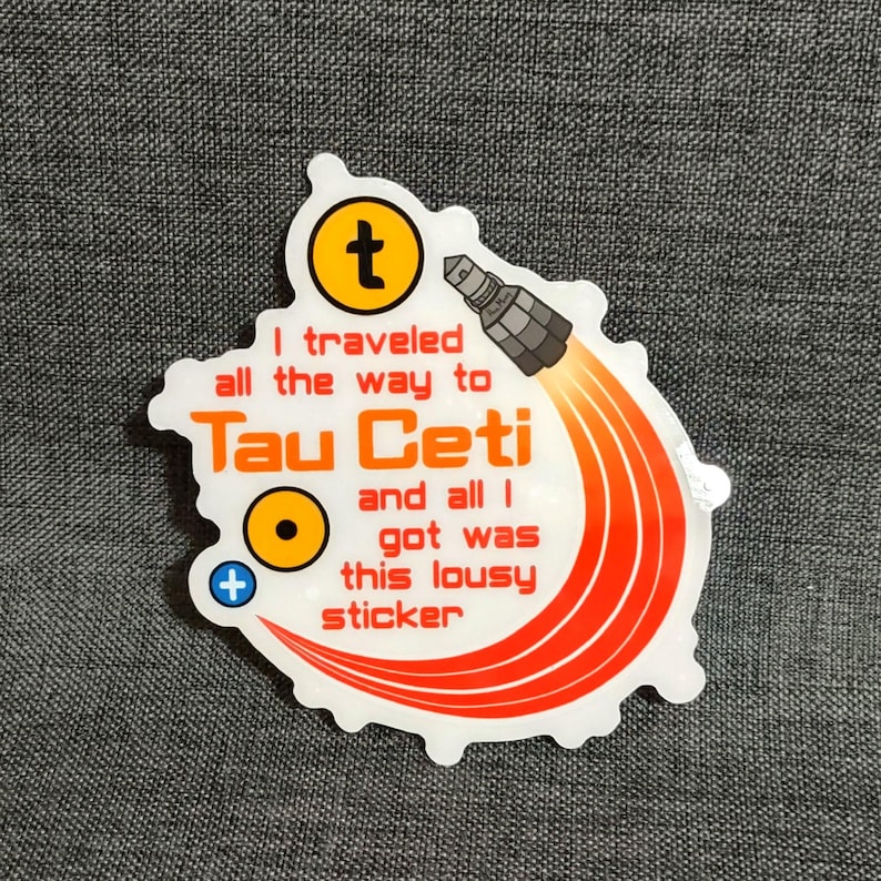 Puede incluir: Pegatina blanca con el texto "I traveled all the way to Tau Ceti and all I got was this lousy sticker." La pegatina tiene un gr&aacute;fico de cohete con llamas naranjas y un s&iacute;mbolo "t" amarillo.