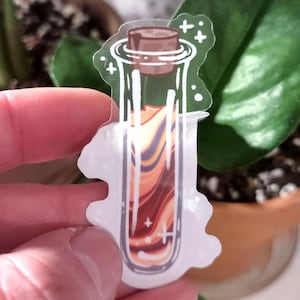 May include: A clear sticker featuring a potion bottle with a cork. The bottle contains layered orange, brown, and purple liquid. White accents and a white outline surround the bottle, with a few small crosses.