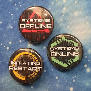 以下が含まれることがあります： テクノロジーをテーマにしたデザインの丸いボタンが3つ。1つのボタンには、赤と黒の背景に白い文字で「SYSTEMS OFFLINE」と書かれています。別のボタンには、緑と黒の背景に白い文字で「SYSTEMS ONLINE」と書かれています。3つ目のボタンには、黄色と黒で「INITIATING RESTART」と書かれています。