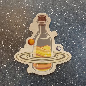 May include: A sticker featuring a clear bottle with a cork, filled with layers of yellow and orange liquid. The bottle is surrounded by a planet with rings and two smaller planets, all set against a starry background.
