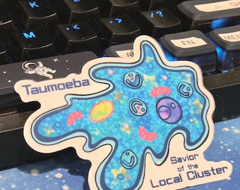 May include: A die-cut sticker featuring a blue, amoeba-like organism with a holographic star pattern. The text reads Taumoeba and Savior of the Local Cluster. The design includes various internal cellular structures in pink, yellow, and purple.