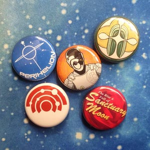 May include: Five circular badges with diverse designs. One is blue with "PERIHELION" and a white graphic. Another is red with "The Rise & Fall of Sanctuary Moon". Other badges feature abstract art.