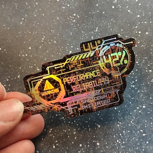 May include: A holographic sticker with a futuristic design. The sticker features the words "WARNING", "PERFORMANCE RELIABILITY", and "SHUTDOWN INITIATED". It also displays a percentage of 42%. The sticker has a black and orange colour scheme.